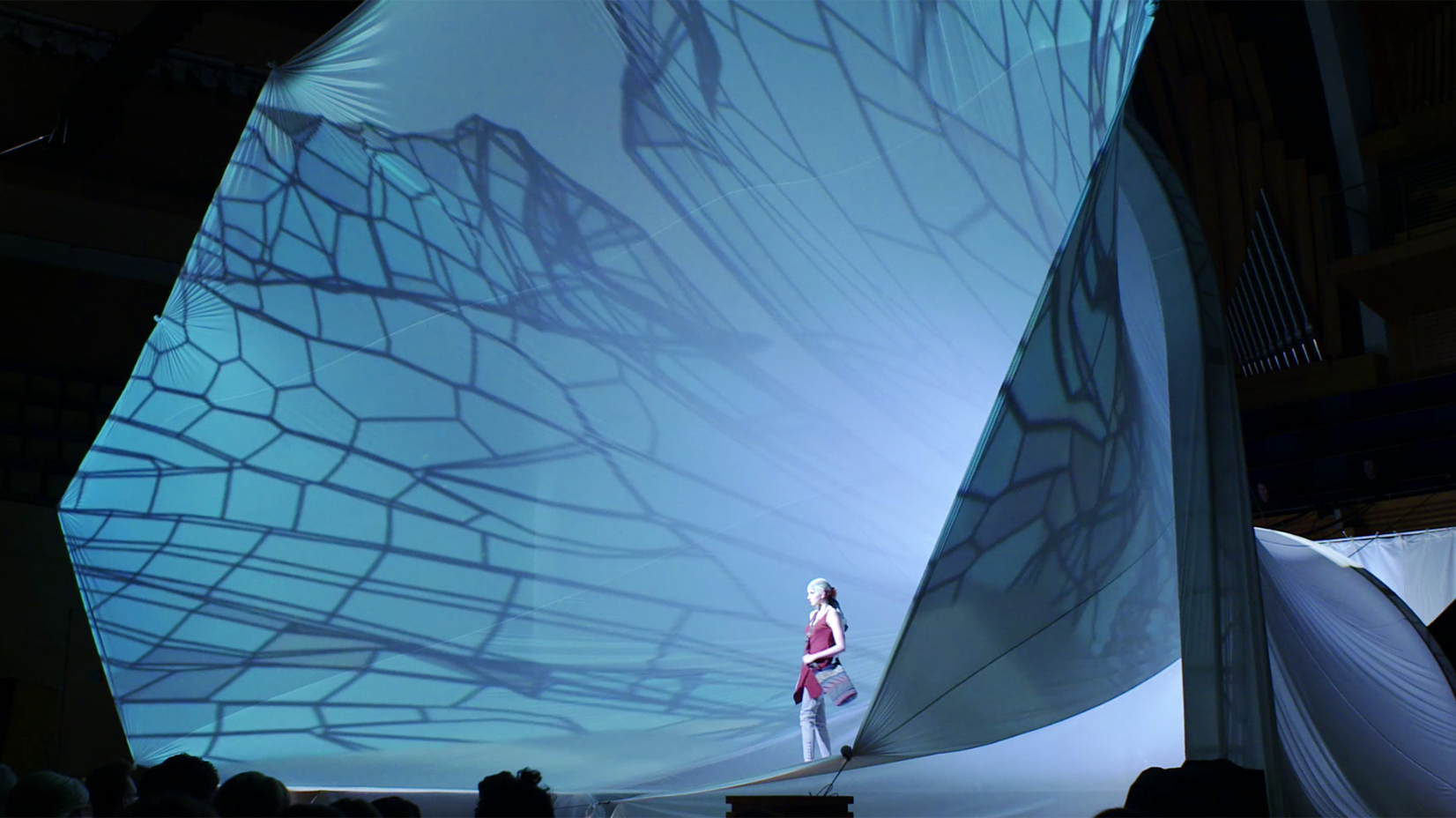 A woman walking a runway during a fashion show with a gigantic projection of wings