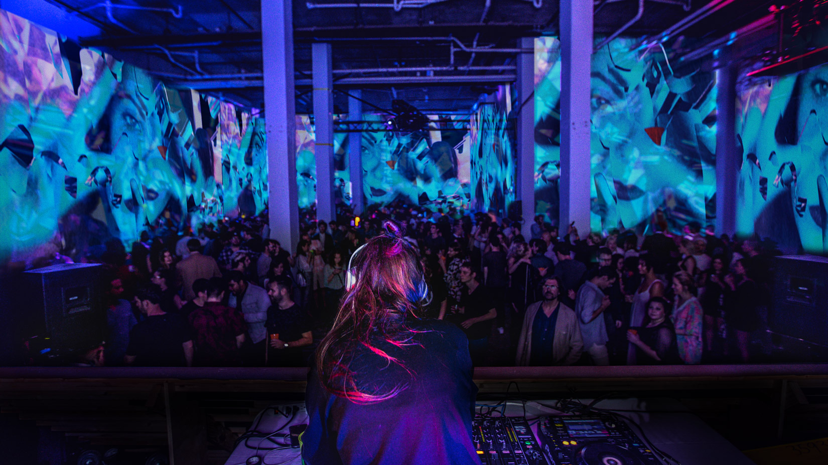 A DJ in front of a crowd of people with projection mapping on all of the walls of people's faces