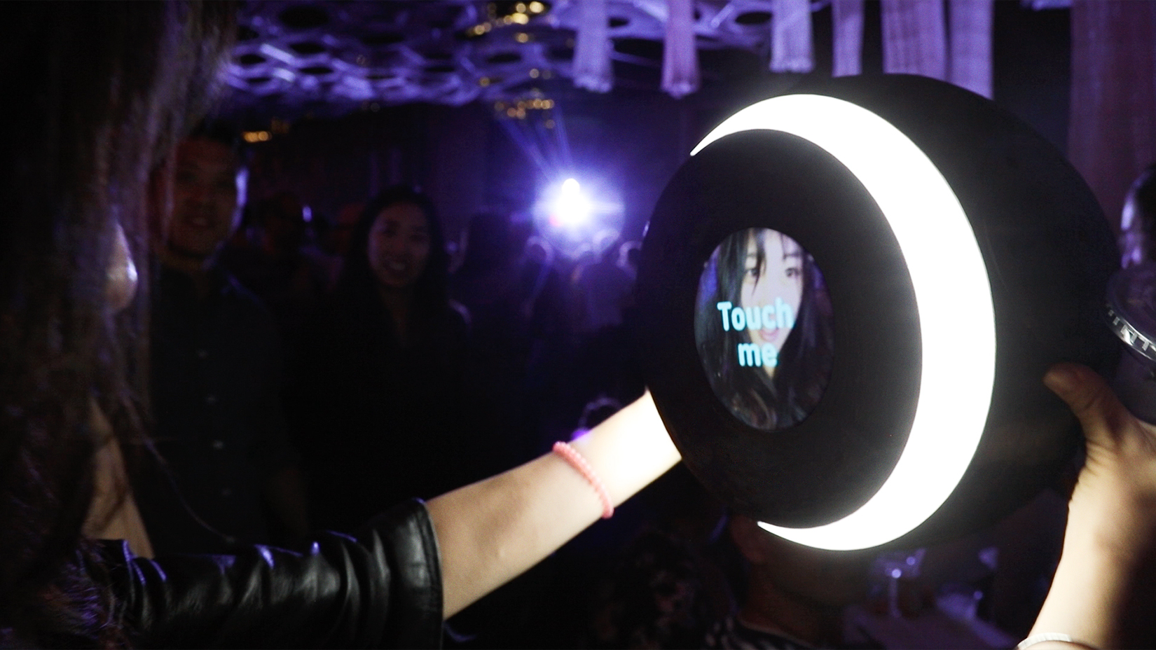 A person holding a sphere with a ring light and a camera, looking at their image on the screen