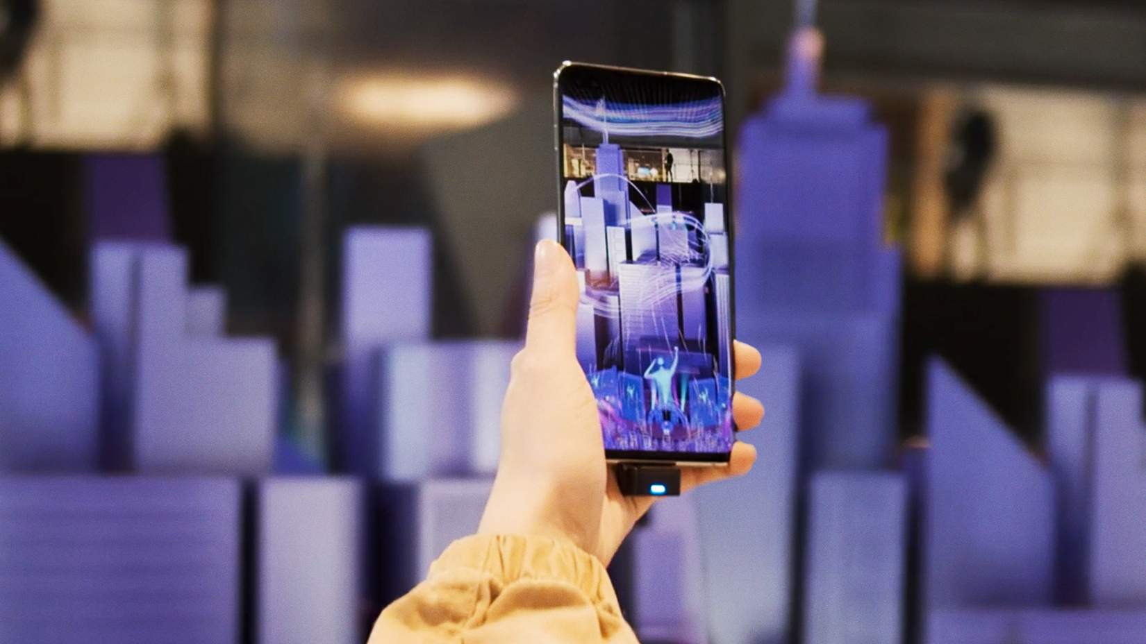 A person's hand holding a phone with AR graphics on a purple art installation for Samsung